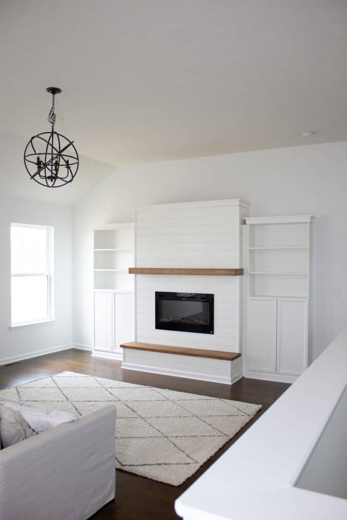 a living room featuring a custom built modern farmhouse electric fireplace feature wall with attached IKEA Billy bookcases, floating mantle, and a wooden hearth