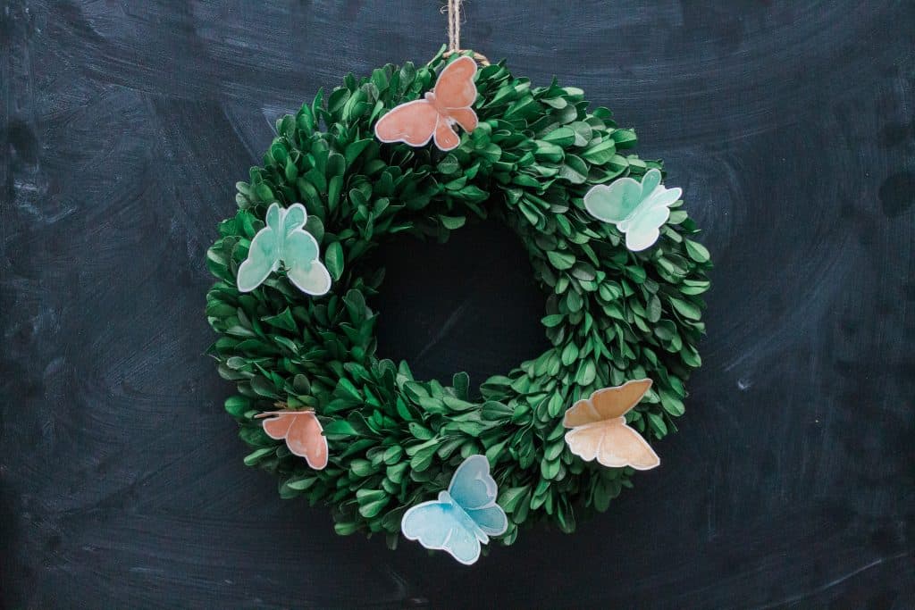 close-up view of preserved boxwood wreath with watercolor butterflies hanging on a chalkboard