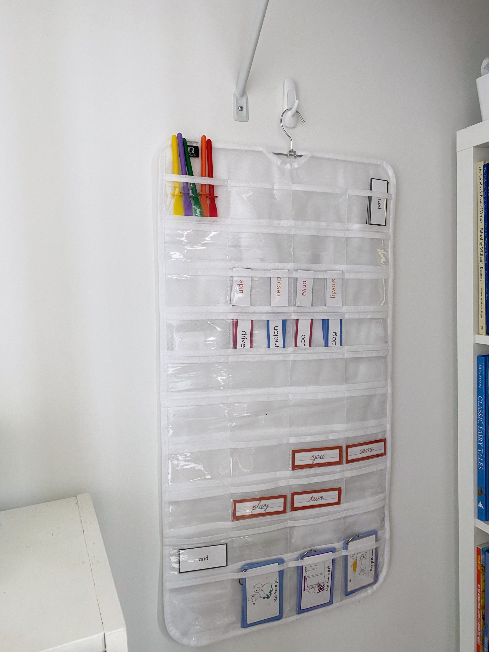 A hanging jewelry organizer stores reading and grammar materials in a Montessori-inspired homeschool space. 